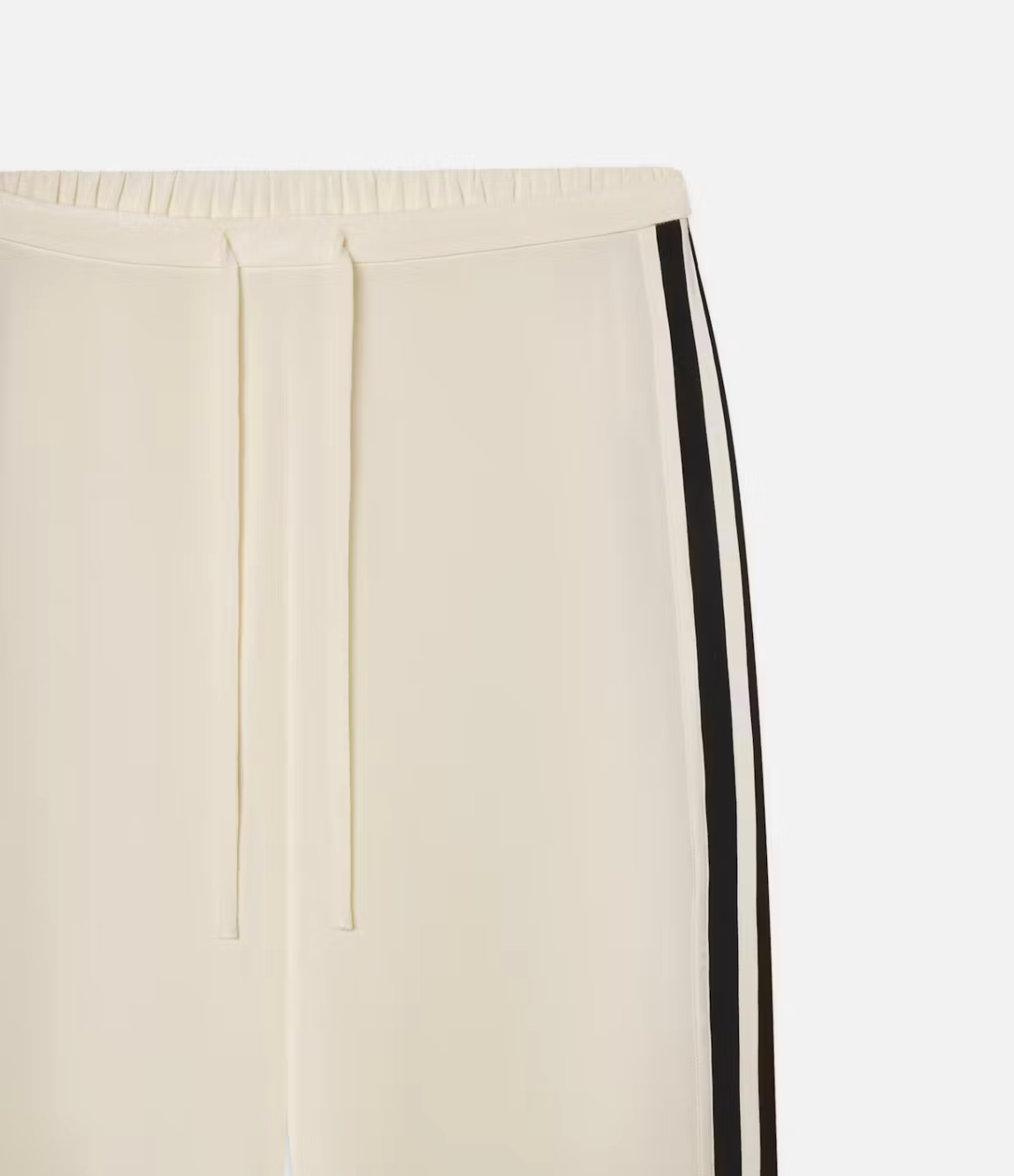 The FRAME Silk Pajama Pant features light beige silk with an elastic waist and drawstring, detailed by a black vertical stripe on the sides. The smooth, lightweight fabric gives it a fluid silhouette.