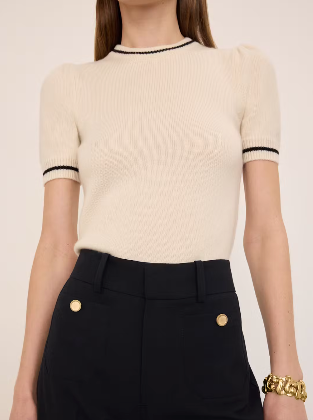 Wearing a FRAME Cashmere Gathered Sweater paired with high-waisted black pants creates an elegant, feminine look. Complementing this ensemble is a chunky gold bracelet that adds sophistication and draws attention.