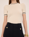 Wearing a FRAME Cashmere Gathered Sweater paired with high-waisted black pants creates an elegant, feminine look. Complementing this ensemble is a chunky gold bracelet that adds sophistication and draws attention.