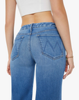 Rear view of someone wearing Mother’s The Roller Fray high-waisted wide leg blue jeans with embroidered back pockets and a white crop top. The mid-blue wash denim pairs perfectly with the bracelet on the right wrist, adding flair to the look.