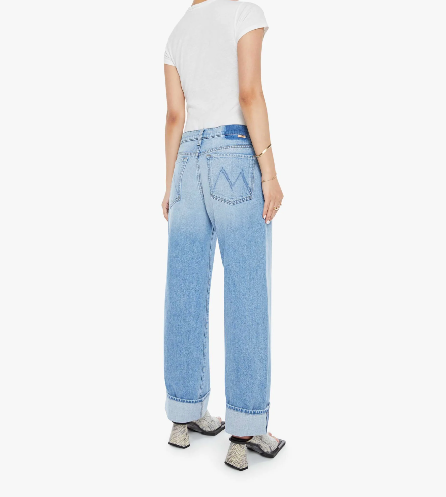 Rear view of a person in Mother Lil Dodger button Hover Cuff jeans with a loose fit and faded blue detail, styled with a plain white t-shirt and snakeskin-patterned shoes. Ideal for petite body types seeking stylish comfort in SUPERIOR denim. Arms are relaxed by their sides.