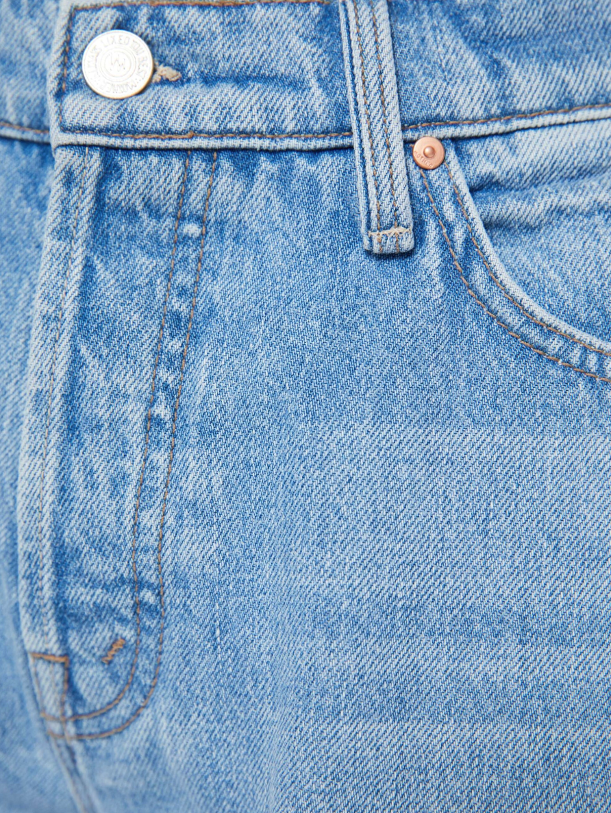 Close-up of Lil Dodger button Hover Cuff by Mother in blue denim, showcasing its texture, stitching, and metal button. The visible pocket and belt loop highlight the classic design and detailed craftsmanship typical of slouchy fit jeans.