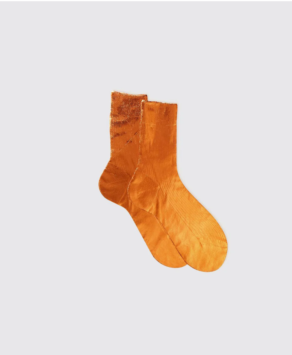 Two Flash Socks by Maria La Rosa, made from silk yarn in orange velvet, are set against a plain gray background. The soft and shiny texture is evident as the socks overlap with one slightly behind the other.