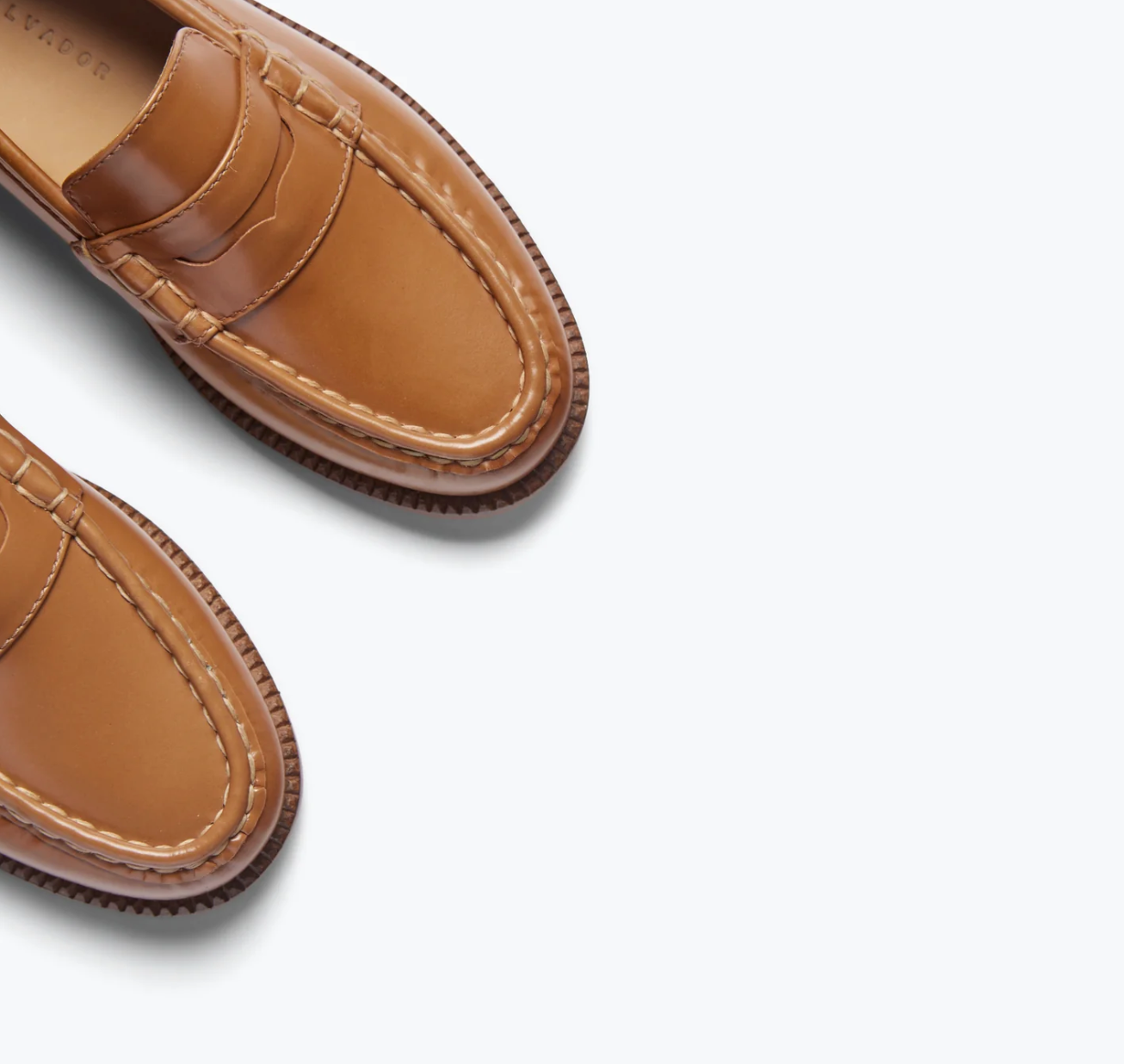 A close-up showcases the ELBA Loafer by Freda Salvador against a plain white backdrop. Handcrafted from Italian leather, they boast a light brown hue with classic stitching and a polished finish, highlighting their elegant and timeless design.