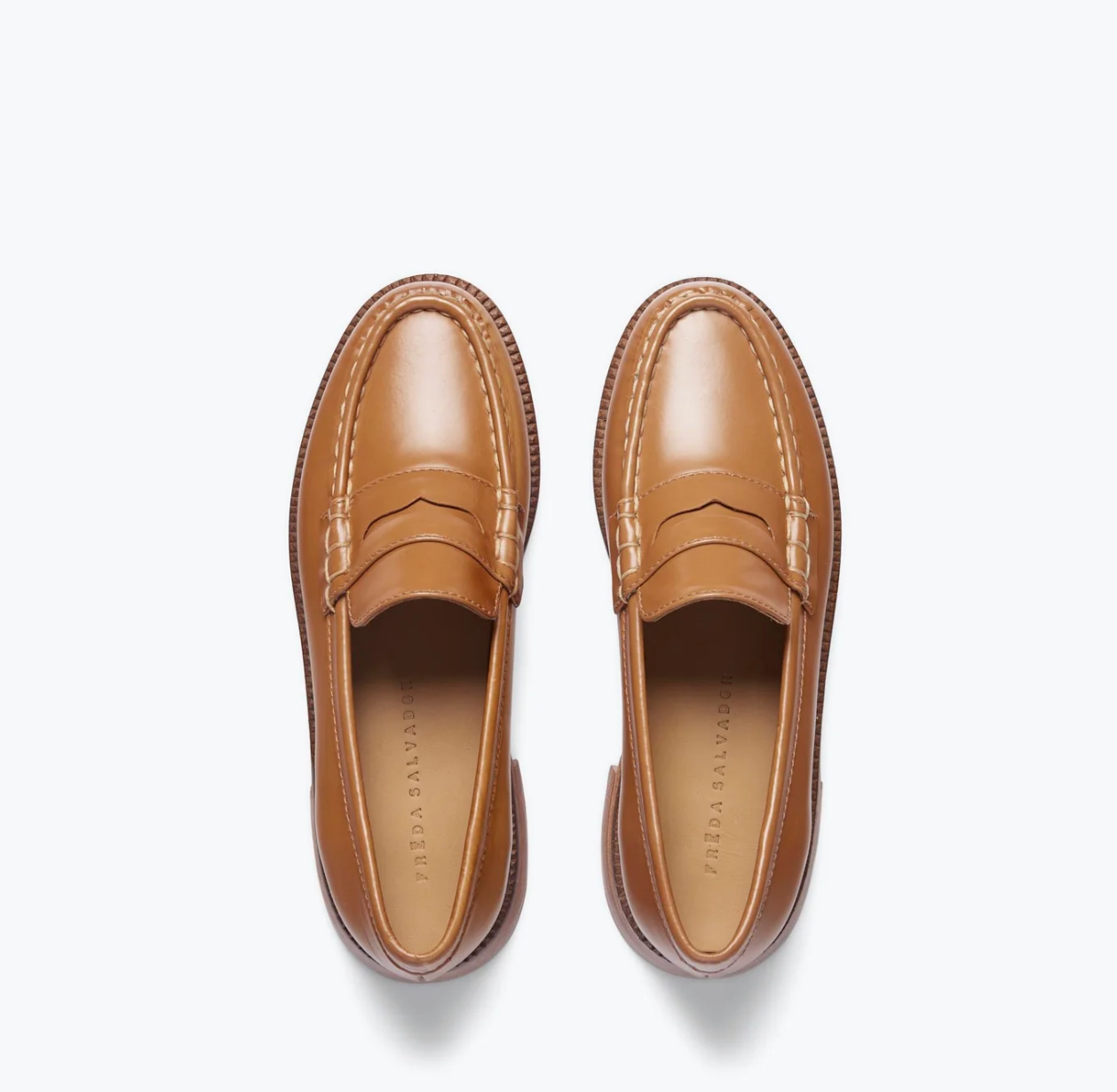 The ELBA Loafer from Freda Salvador is a pair of handcrafted brown leather shoes with a polished finish and moc toe design. They feature a penny loafer strap, visible insoles with printed text, and are displayed against a white background.