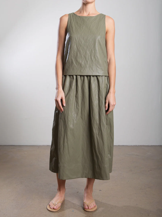 Wearing Pharaoh's Claudia Skirt and a sleeveless olive green top, the person stands against a light background. The chic ensemble, made of textured fabric with matching midi skirt and elastic waist, is paired with sandals and crafted in Los Angeles.