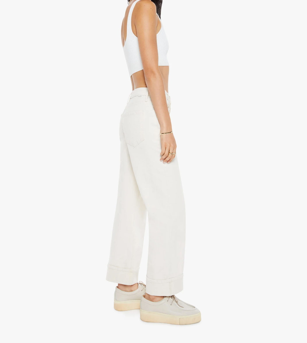 A person in a white crop top and wide-legged white pants, made from a superior cotton blend, stands in profile against a plain backdrop. They wear beige platform sneakers and have their wrist adorned with several bracelets, including The Spitfire Ankle Cuff by Mother.