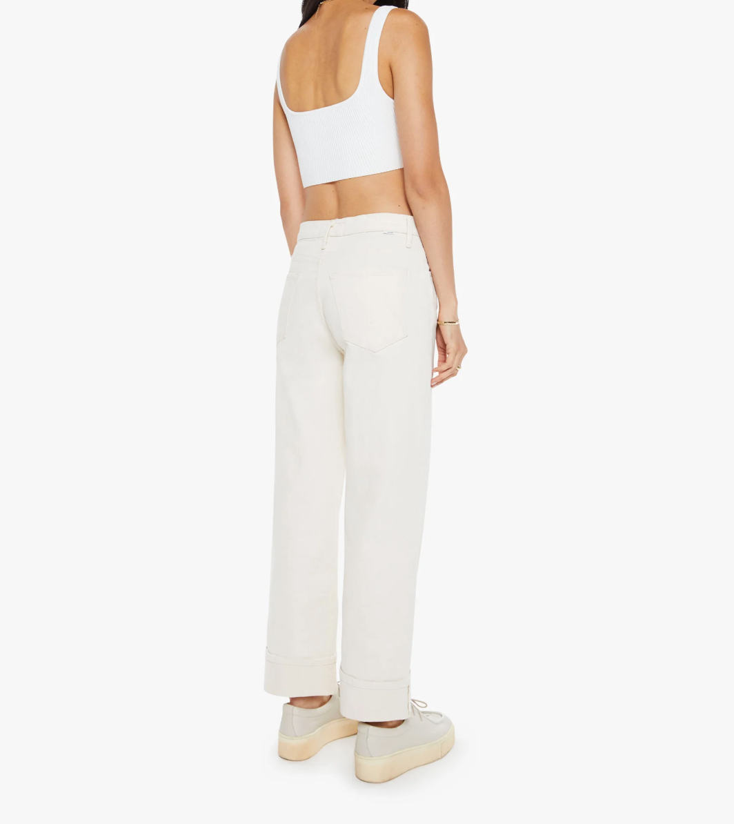 Rear view of a person wearing light-colored sneakers, Mother brand's The Spitfire Ankle Cuff jeans, and an oversized-fit white crop top. The jeans add charm with their high waist and wide legs, rolled cuffs flaunting the plain white background. Crafted from a soft cotton blend.