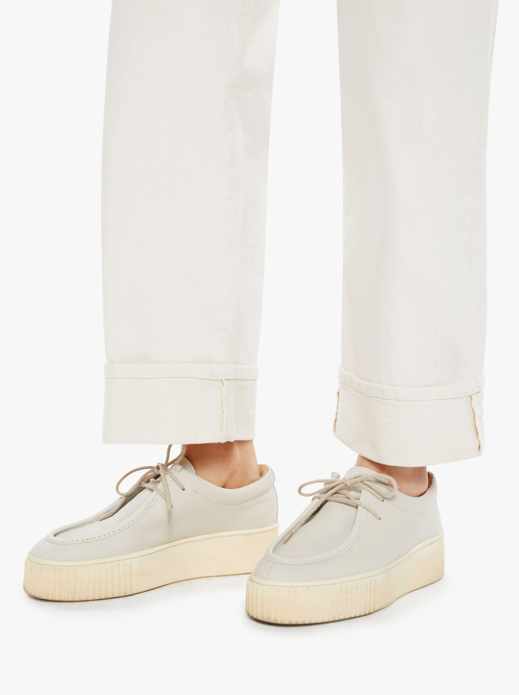 A person wears The Spitfire Ankle Cuff by Mother, cream-colored platform sneakers with beige soles and laces, paired perfectly with white cuffed pants in a SUPERIOR cotton blend. Set against a plain white background, the ensemble exudes a modern yet timeless appeal.