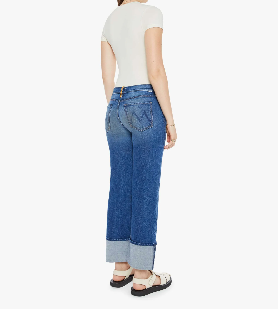 A person models the Mother Checkerboard Duster Flood Cuff high rise jeans with rolled cuffs and distinctive back pocket stitching, paired with a white fitted top and sandals against a plain white background.