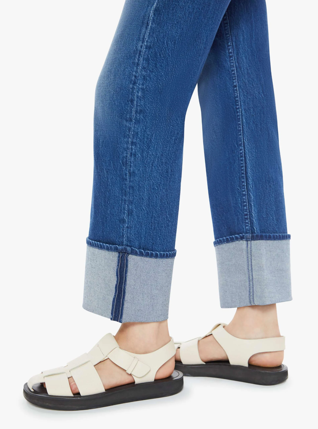 A person stands against a plain background wearing the Checkerboard Duster Flood Cuff from Mother with rolled-up hems and beige strappy sandals featuring black soles.