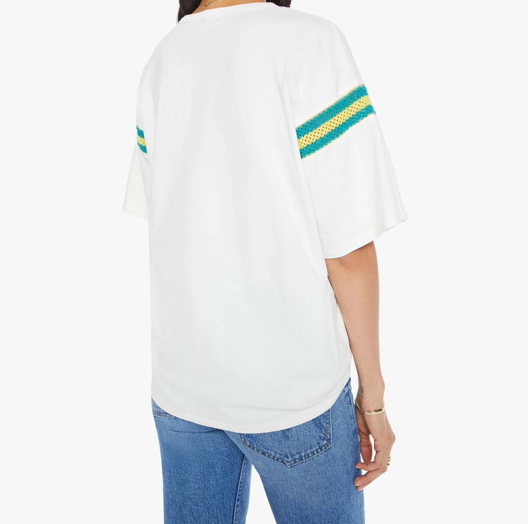 A person wearing The Sleep Over Inset by Mother—a white 100% cotton oversized T-shirt with green and yellow striped sleeves—is shown from the back, paired with blue jeans and a bracelet, creating the perfect sleep-over vibe against a plain white backdrop.