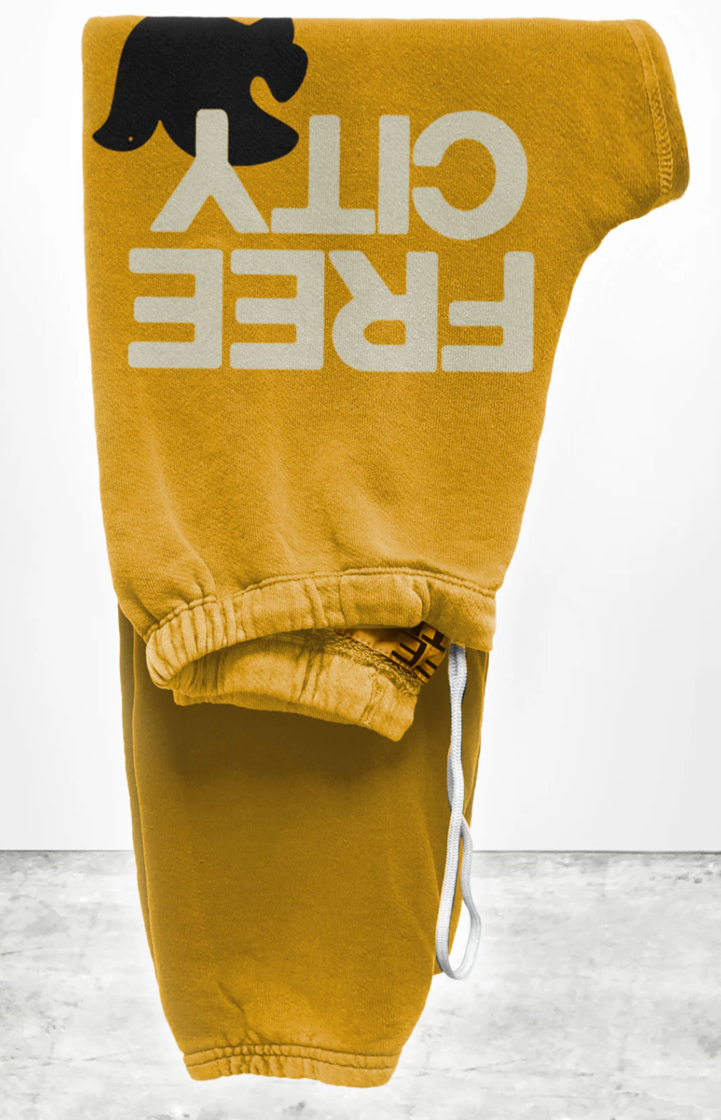 The FREECITY Large Sweatpant by Free City (sparrow, LLC) in yellow is a unisex design crafted in the USA from lightweight French terry. It features an elastic waistband with a white drawstring, "FREE CITY" text, and a bird silhouette. Displayed elegantly on a light gray surface.