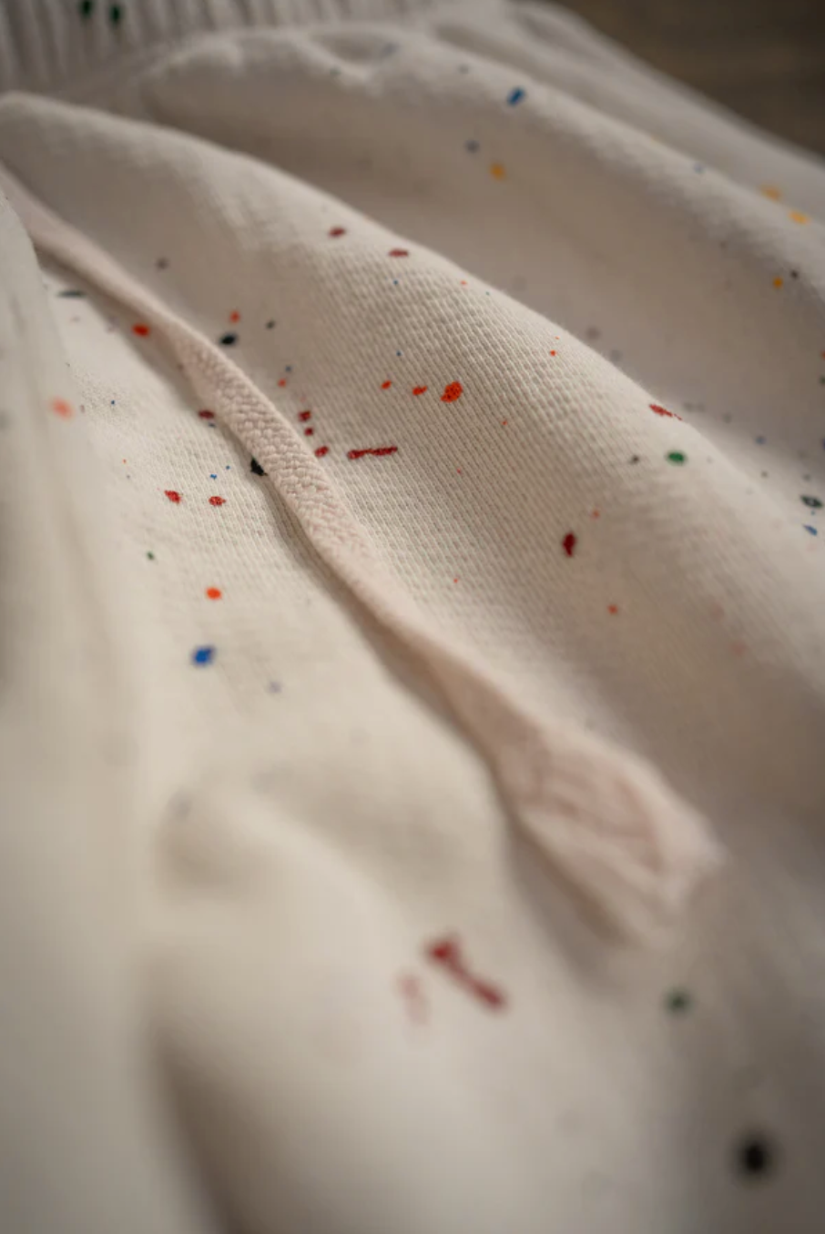 Close-up of a PE Sweatpant by Made Worn, crafted from white French terry cotton with a drawstring and multicolored paint splatters, evoking vintage sweatpants.