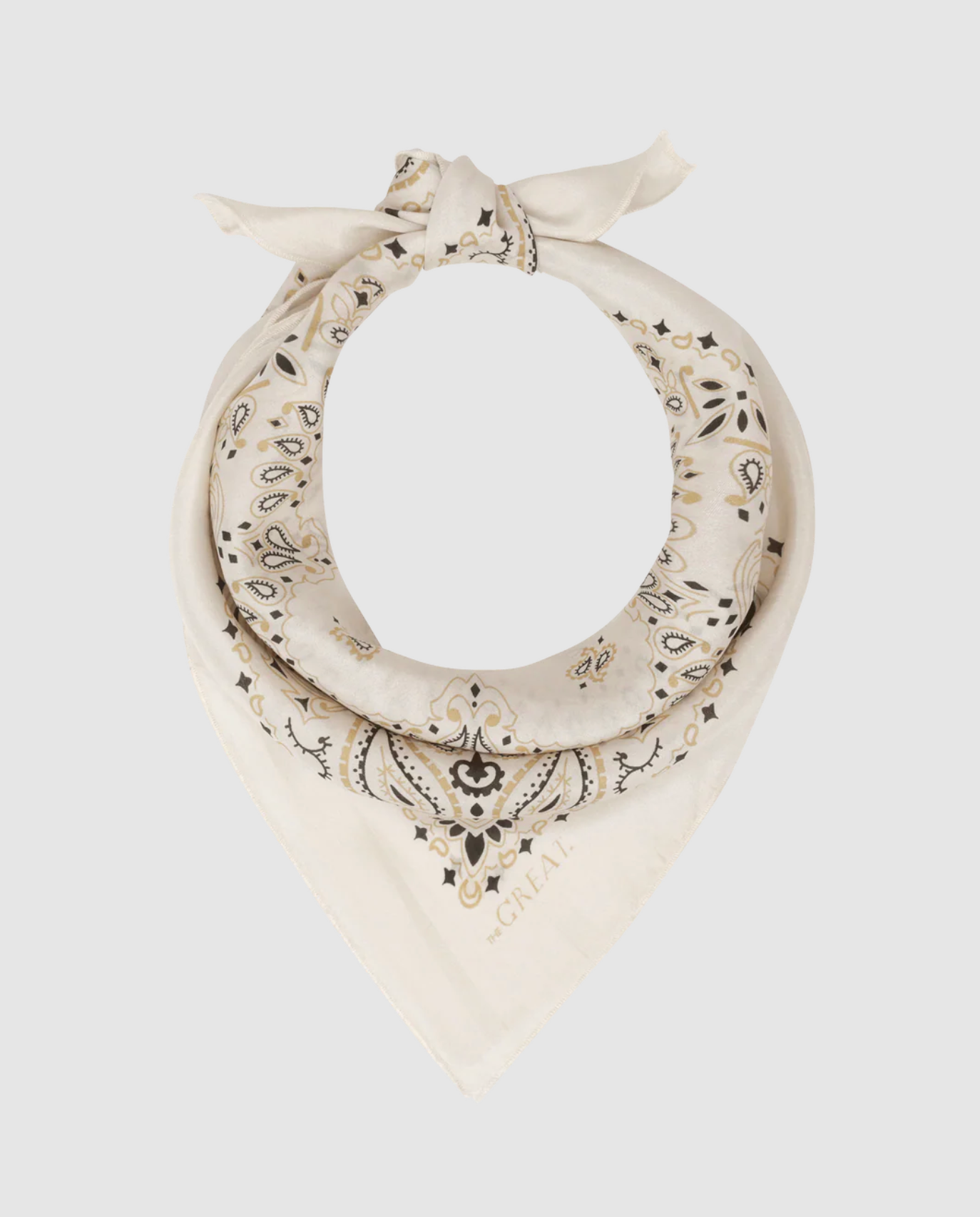 The Great Inc.’s The Silk Bandana, in cream silk with black and gold paisley patterns, is tied in a loose knot and displayed on a plain light gray background.