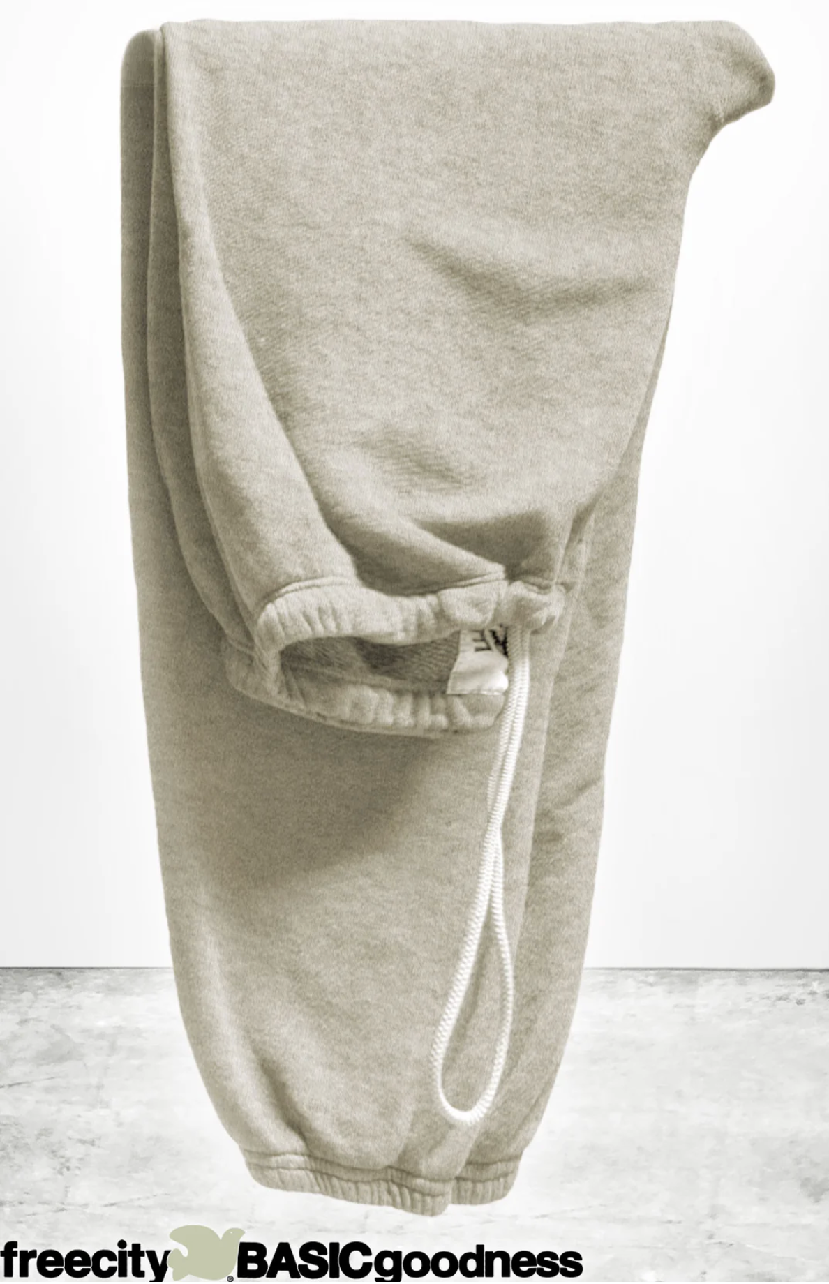 A pair of light gray BASIC GOODNESS OG SWEATPANTS by Free City (sparrow, LLC) is folded over a surface with a white drawstring. The background is plain, and "freecity BASICgoodness" appears at the bottom.