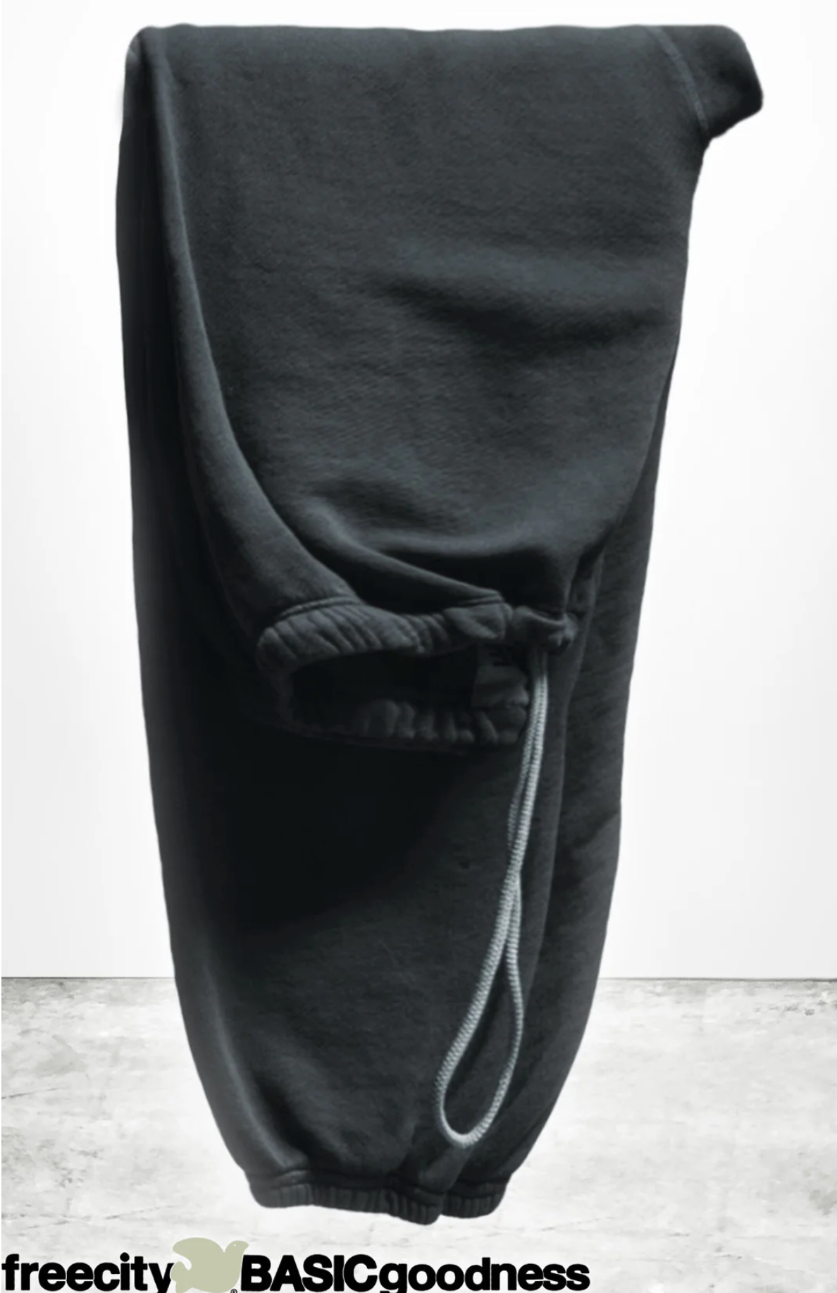A pair of BASIC GOODNESS OG SWEATPANTS by Free City (sparrow, LLC), in black French terry and made in the USA, is folded with one leg over the other. An elastic waistband with drawstring and a “freecity BASICgoodness” logo are visible.