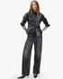 A woman stands with hands in her pockets, wearing a black leather button-up shirt, Rag & Bone Miramar Drawstring Wide-Leg Pants, and black pointed-toe heels against a plain white background.