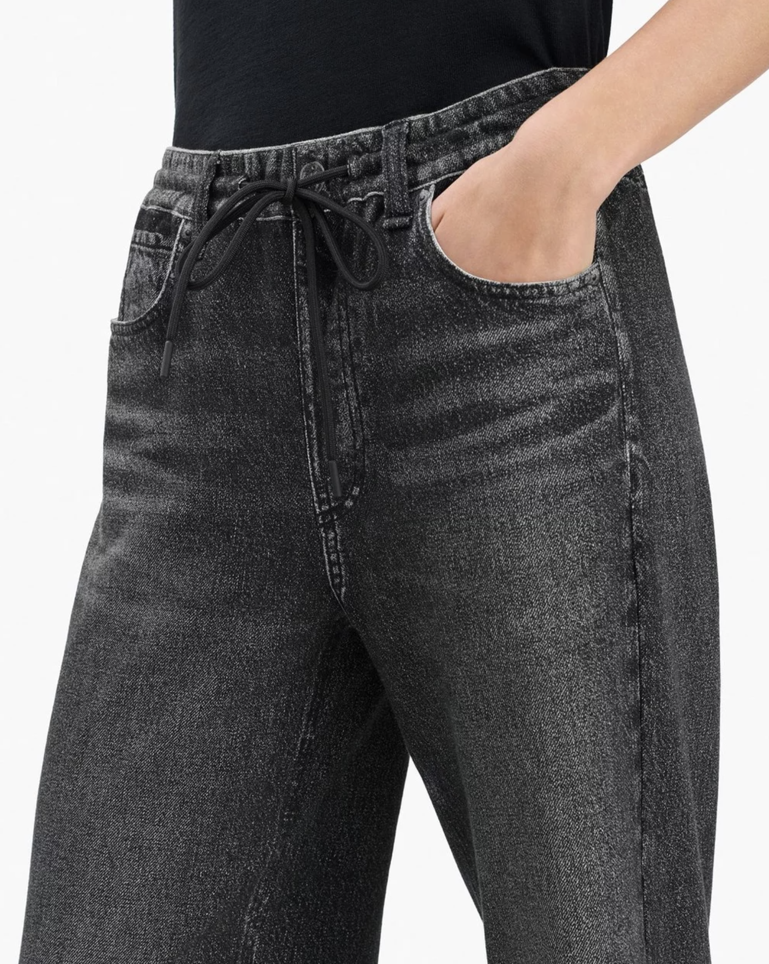 A person wears Rag & Bone Miramar Drawstring Wide-Leg Pants—high-waisted, black acid-wash with an elastic waist and front pocket—and a black top.