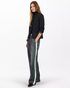 A person with long, light brown hair wears a black blazer, black top, and Rag & Bone's miramar terry track pant pull on with bold white and green side stripes, standing against a plain white background.