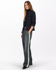 A person with long, light brown hair wears a black blazer, black top, and Rag & Bone's miramar terry track pant pull on with bold white and green side stripes, standing against a plain white background.