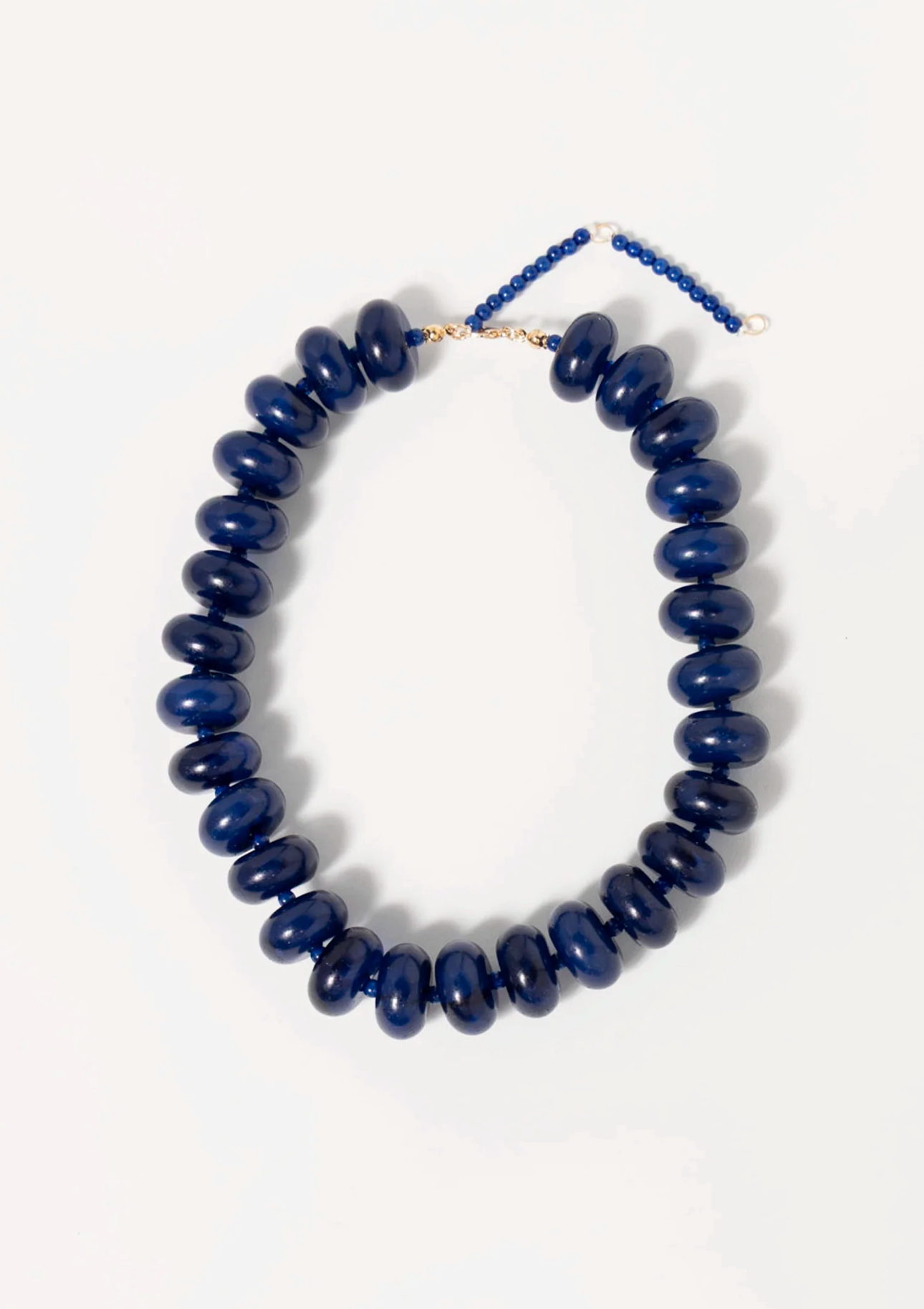 The Bailey Chunky Beaded Necklace by Faire features large, glossy dark blue marbled beads on a thin cord with an adjustable gold-tone clasp and beaded extension, shown against a plain white background.