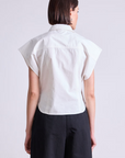 Seen from behind, a person with short brown hair wears the Apiece Apart Toni Sleeveless Top in white organic cotton and black high-waisted pants, creating a modern silhouette against a plain light background.