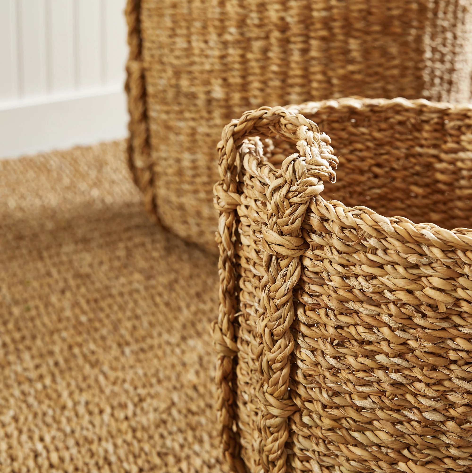 Close-up of two Napa Home & Garden Seagrass Round Drum Baskets with thick braided edges on a textured rug in a bright room—ideal for stylish storage and adding a natural touch.
