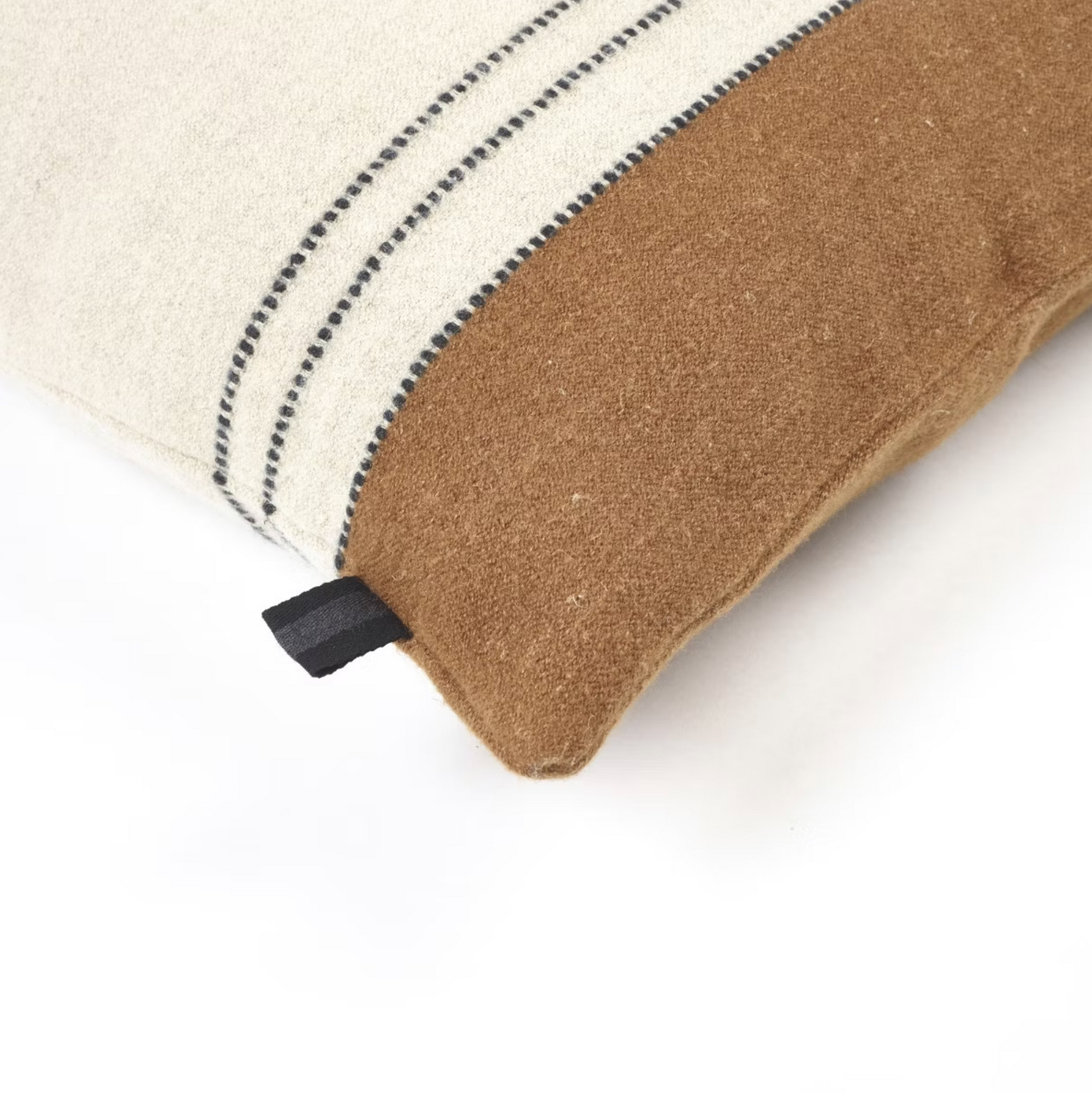 The Foundry Pillow by Libeco Home showcases a cream top with black wool-stitched lines and a solid brown bottom. A small black fabric tag accents the side of this rectangular artisanal pillow, which rests on a white surface.