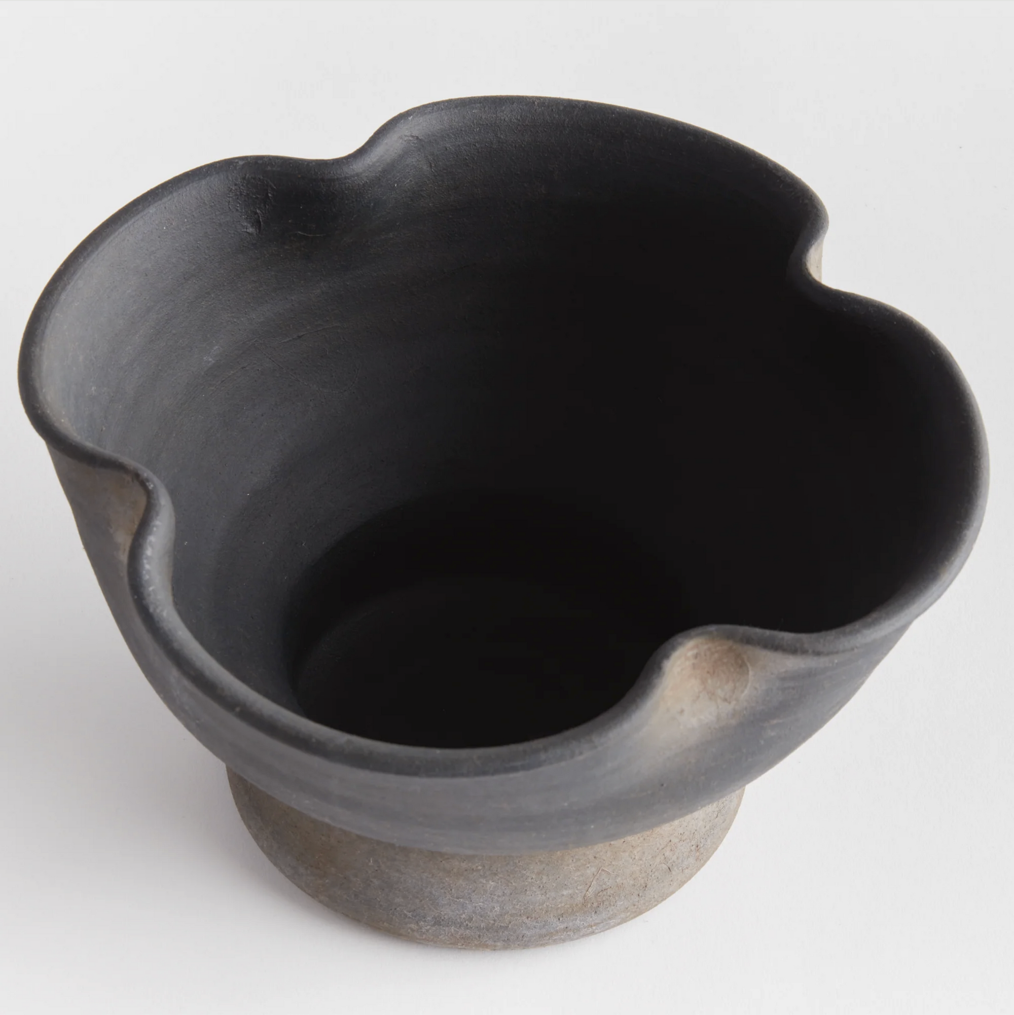 The Kaloa Bowl by Napa Home & Garden is a handcrafted black ceramic piece with a matte finish, rounded base, and four-curved undulating rim, displayed against a plain white background.
