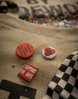 Three pins on the Made Worn Artist Tote: “DIDN’T LIKE COLLEGE ANYWAY,” “SUPPORT THE ARTS,” and a “SLICE MY WAY” graphic. The tan cotton canvas bag also features a black-and-white checkered pattern.