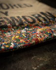 A close-up of the limited-edition Made Worn Artist Tote shows its vibrant paint-splattered cotton canvas, partially displaying bold black text on a tan background and highlighting the rich textured details.