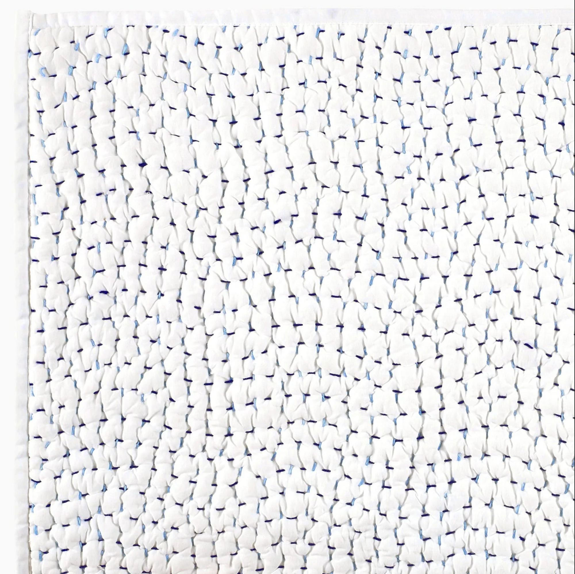 Close-up of the John Robshaw Coverlet Queen: white organic cotton voile with a gathered texture and subtle blue accents. The fabric’s edge appears along the top and left sides.