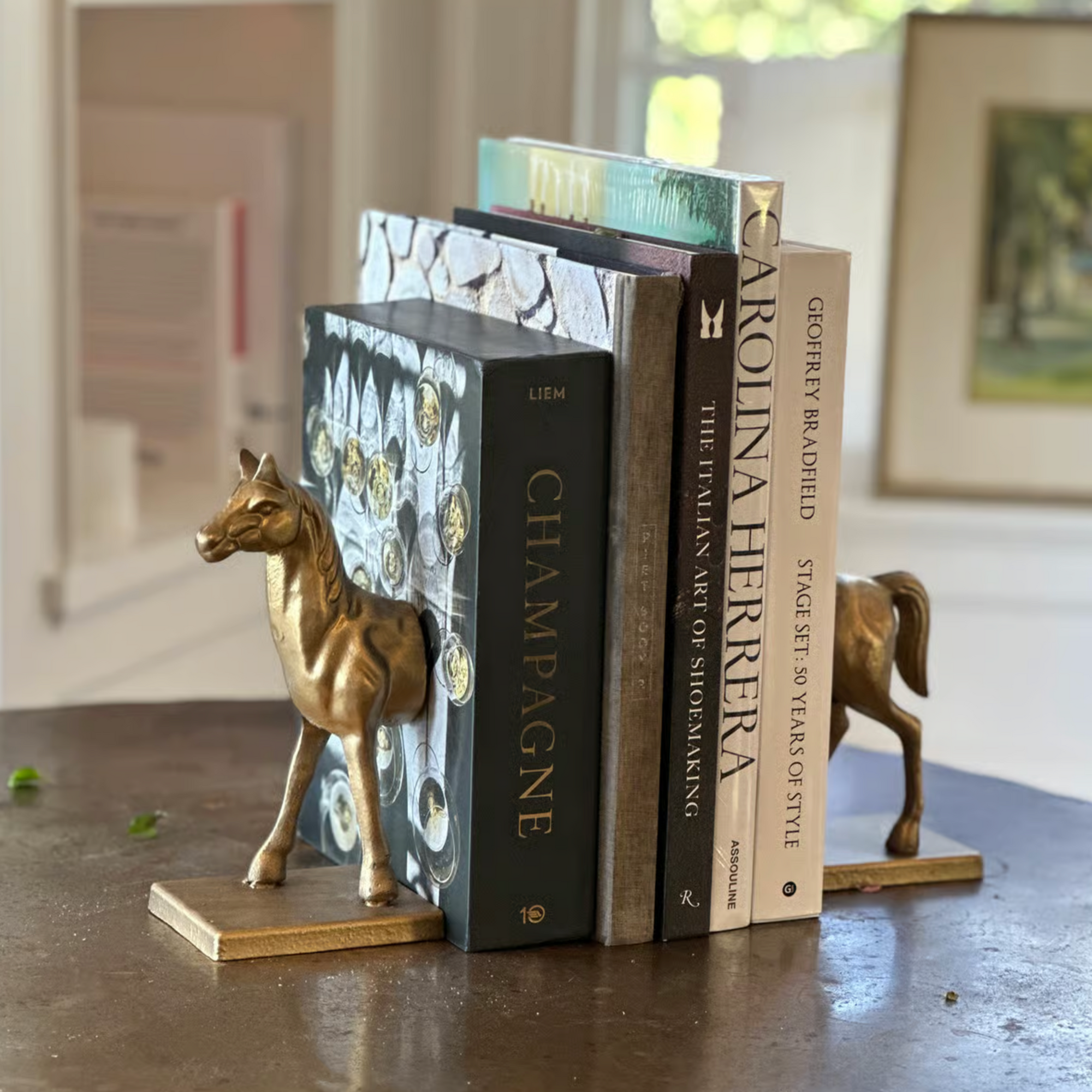 The Fox Run Brands Horse Bookend Set holds up several books, including &quot;Champagne,&quot; on a table in a bright, window-lit room.