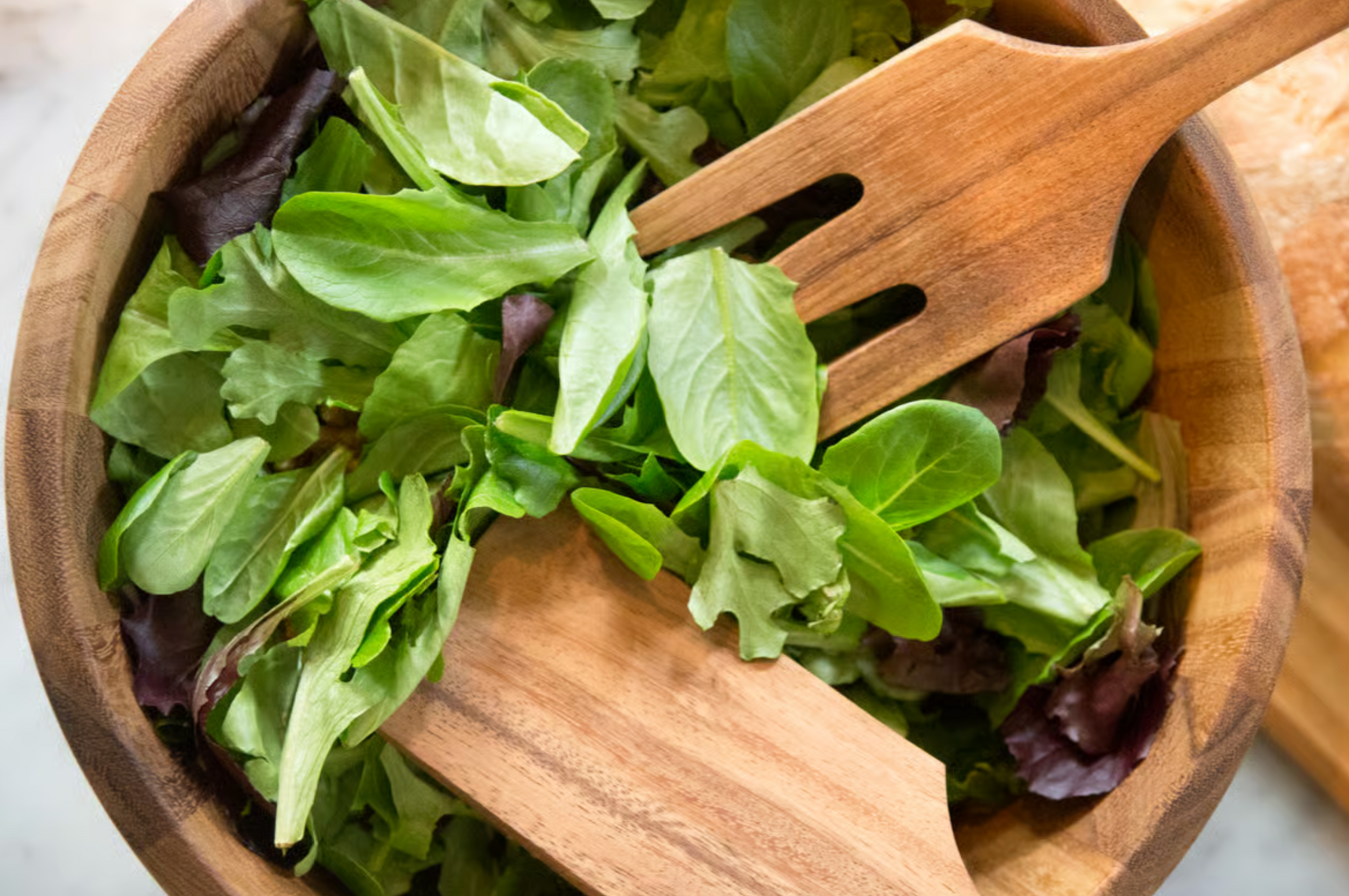 A wooden salad bowl with fresh mixed greens, paired with the Fox Run Brands Acacia Utensil Set crafted from durable Acacia hardwood.