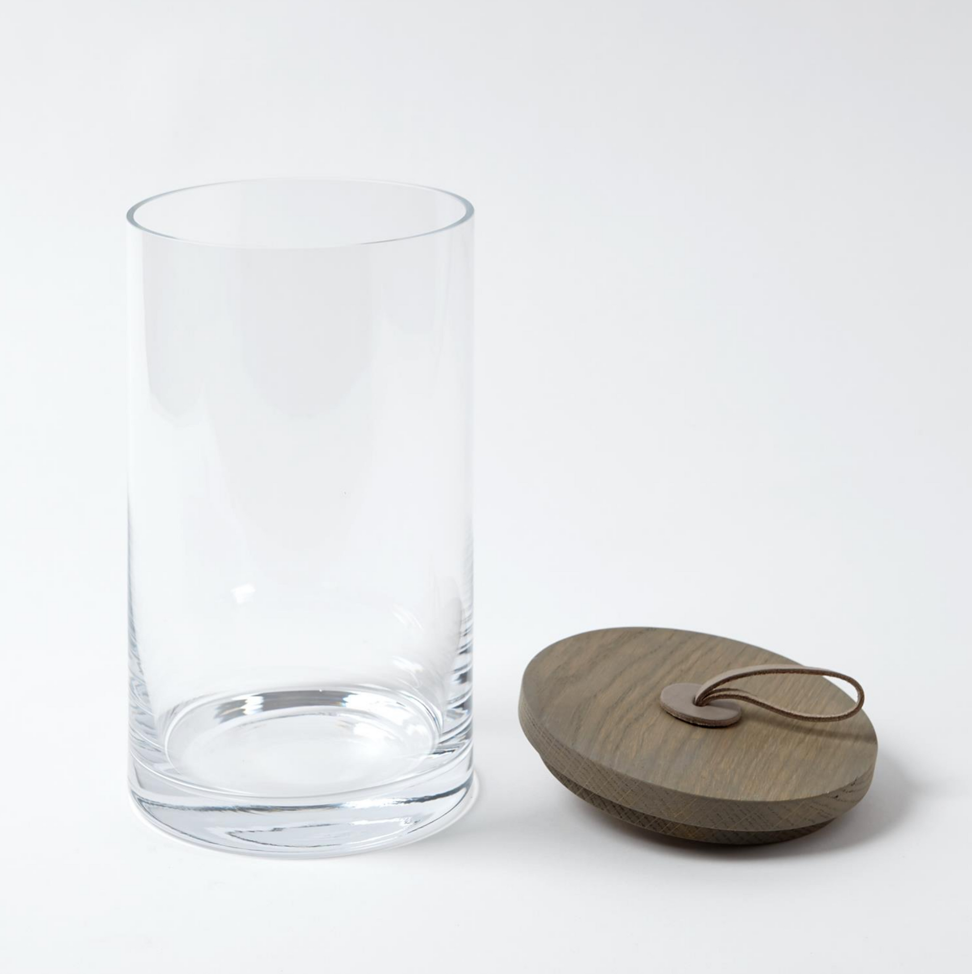 The Rustic Canister LG by Global Views is a clear, cylindrical glass jar with a round wooden lid and leather loop—perfect as a food-safe container for modern or rustic kitchen storage.