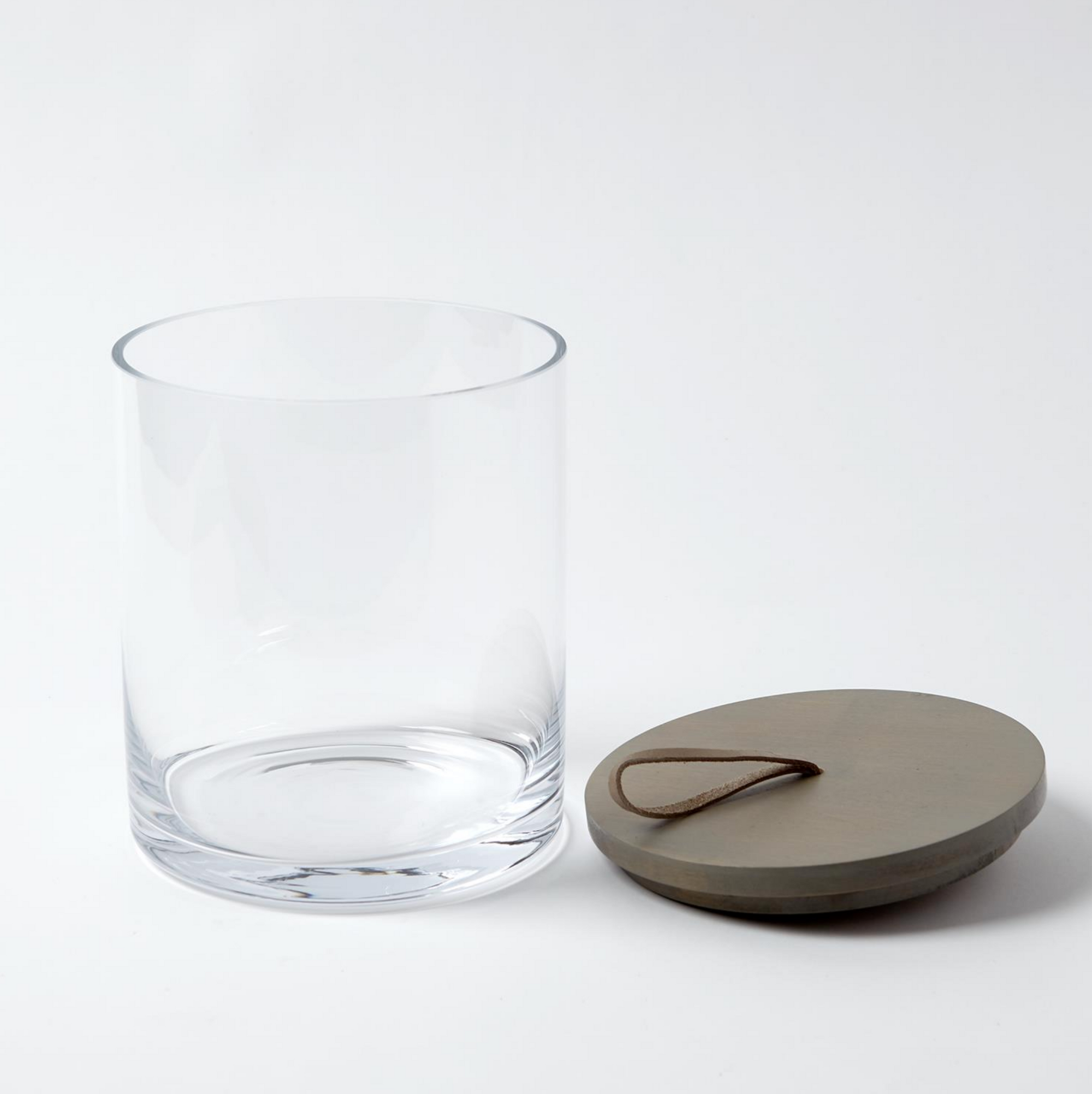 The Rustic Canister MD by Global Views features a clear cylindrical glass jar and a round wooden lid with a leather loop handle, shown on a white background—ideal for rustic kitchen storage or as stylish modern canisters.