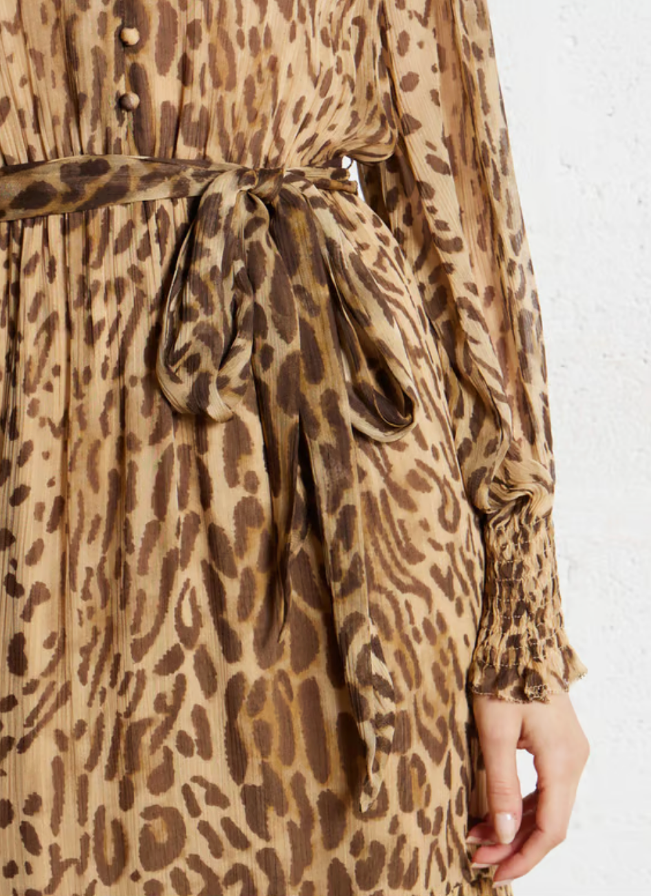 Close-up of a person wearing the SUNCOO Cosmos Dress, a loose-fit brown leopard print dress with a matching fabric belt at the waist. Made from 100% viscose, it has long sleeves with smocked cuffs and the person's hand is at their side.