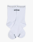 The Half Step by Mother: white ribbed tube socks with metal studs along the top edge and "MOKER" in black near the cuff, crossed and displayed on a plain white background.