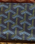 A reusable shopping bag by Faire featuring a repeating geometric pattern of blue and green chevrons on a dark background—designer-inspired and perfect for your next shopping trip.