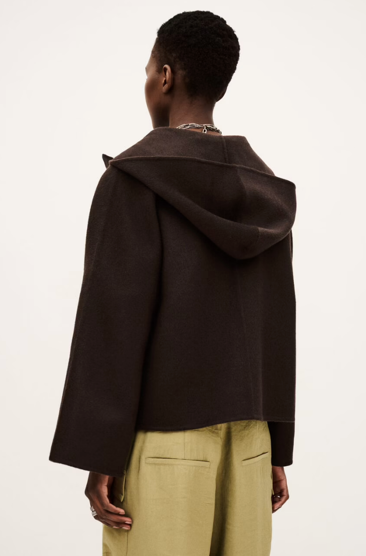 A person with short hair is shown from behind wearing the BA&SH Jacket Kove, a dark brown, loose-fitting style with a wide collar, paired with light green pants against a plain, light background.