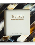 The Black Horn Photo Frame by Two's Company is a square, handcrafted frame with diagonal black, white, brown, and golden-yellow stripes. It features a luxury 4 x 4 inch (10 x 10 cm) display for your photos.