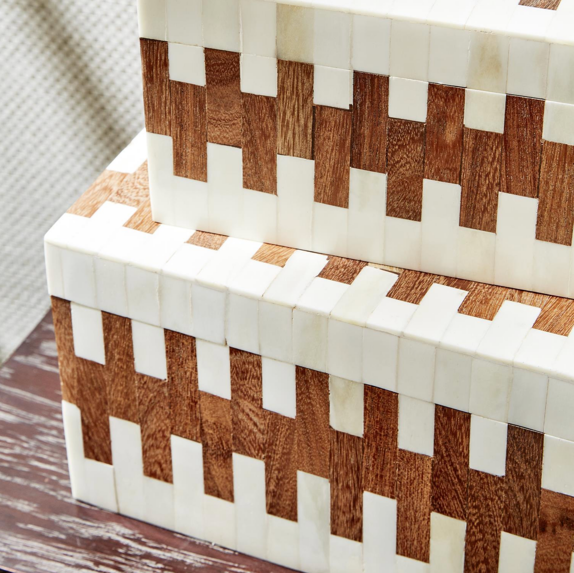 Two's Company JigSaw Covered Boxes, featuring a geometric pattern of alternating light and dark wood-like segments, stacked together on a mottled brown and white surface.
