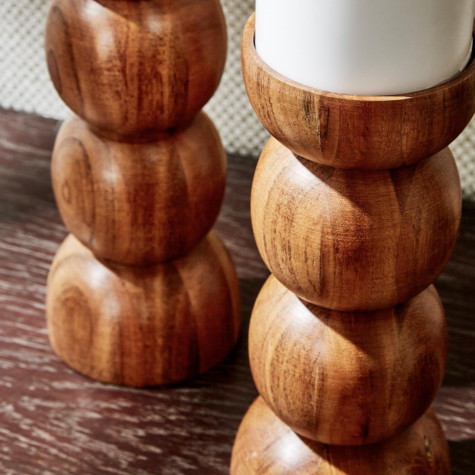 Close-up of two hand-crafted Pillar Candleholders by Two's Company, featuring smooth, rounded shapes and topped with white candles, set on a dark wooden surface for a mid-century modern look.