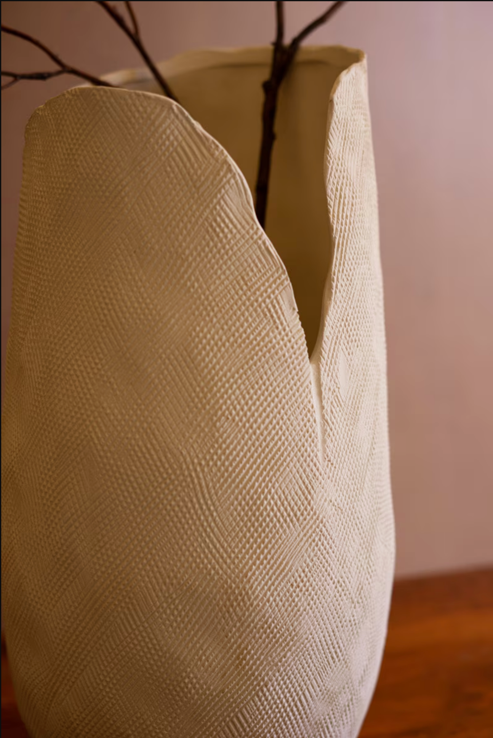 The Bloom Flower Vase L by Kalalou, Inc features a textured cream finish and uneven rim, holding bare branches on a wooden surface against a light, plain background.