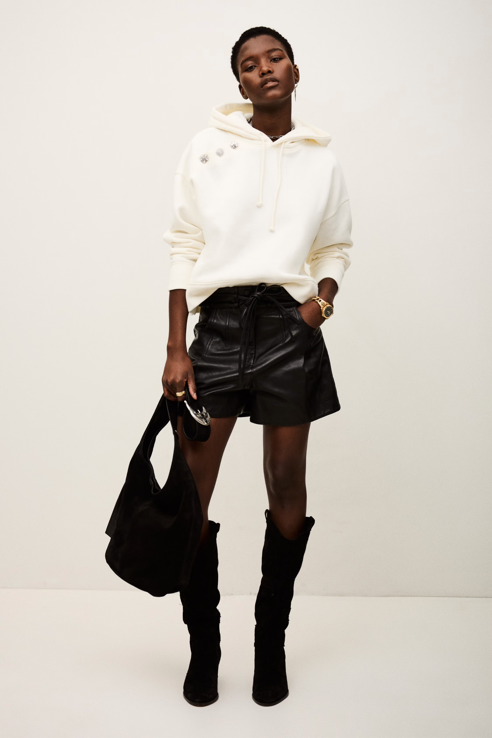 A woman wearing the BA&SH Sweatshirt Didi, a white polyester-cotton blend hoodie, paired with black shorts.