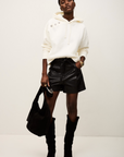 A woman wearing the BA&SH Sweatshirt Didi, a white polyester-cotton blend hoodie, paired with black shorts.