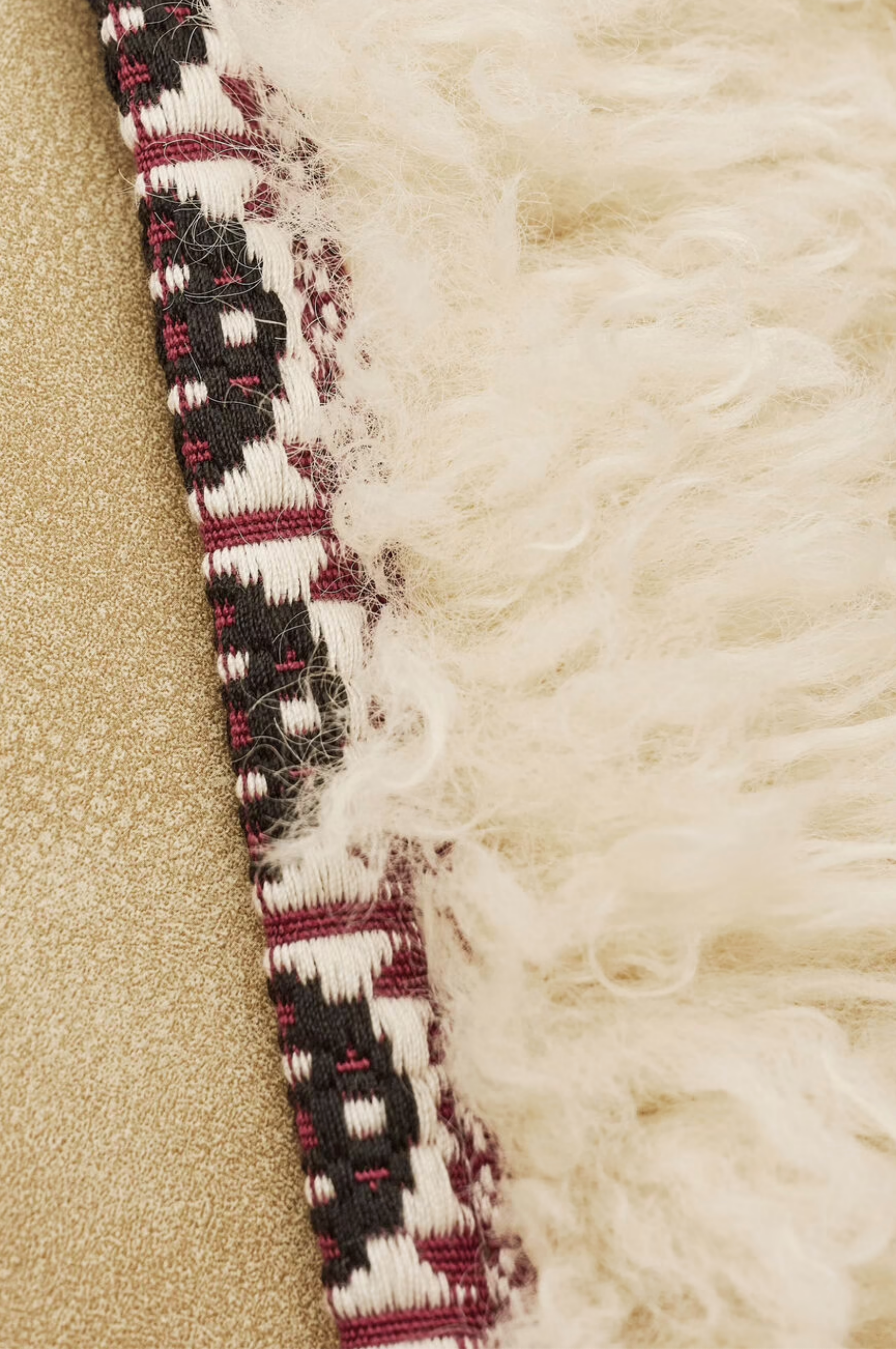 Close-up of the Jacket Celton by BA&SH: beige textured polyester with fluffy off-white fringe, bordered by a woven geometric black, white, and burgundy band. This washable jacket offers easy care with no ironing needed.