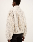 Someone stands facing away, wearing the BA&SH Coat Saros—a printed faux fur cropped jacket with grey animal prints—paired with black jeans against a plain light background.