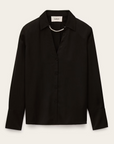 The BA&SH Shirt Itsey is a long-sleeve black button-up blouse with loose-fitting shoulders, a collar, and a subtle sheen, styled with a delicate pearl necklace draped across the collar.